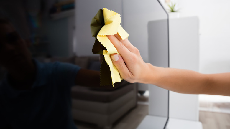 A woman's hand with a soft cloth cleaning a TV screen.