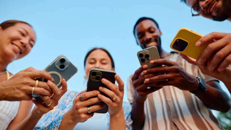Four people smiling while holding iPhones, shown from a low angle that focuses on the phones.