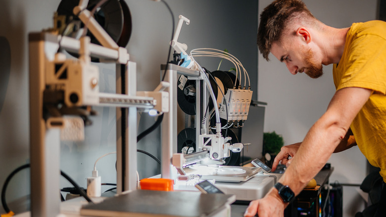 A person standing in front of a 3D printer, looking at a screen