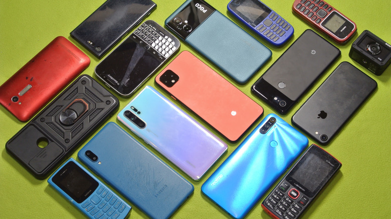 Various old phones on a table, including iPhone, Android, BlackBerry, and dumb phones.