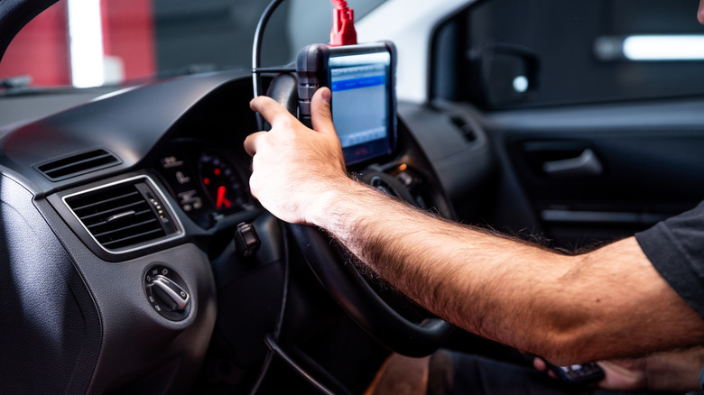 A car technician plugs a tablet device into a car dashboard to install a software update