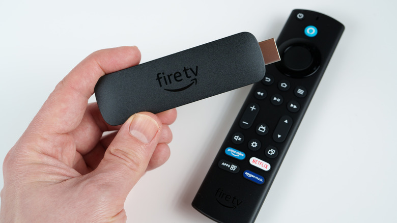 A hand holding an Amazon Fire TV Stick with the remote