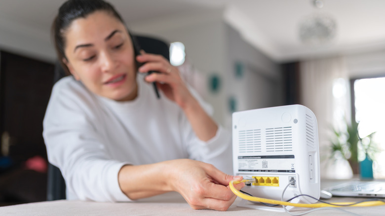 A woman on the phone plugs in her white Wi-Fi router.