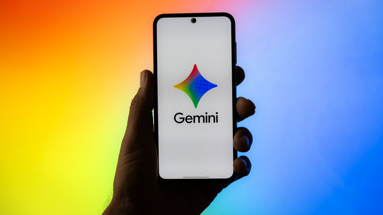 Smartphone held up with Google Gemini logo onscreen and a colorful background.
