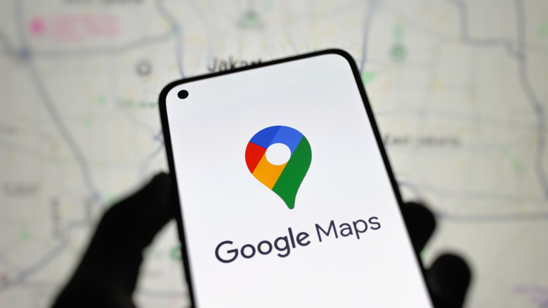 The Google Maps logo displayed on a smartphone with a physical map is in the background