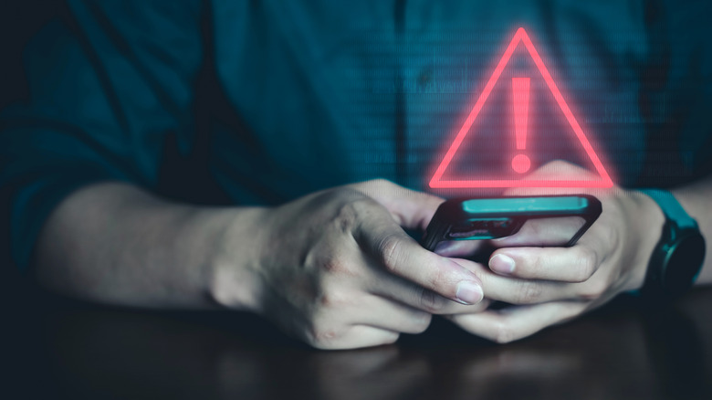 Hands holding a smartphone, above which is a visual effect indicating a warning