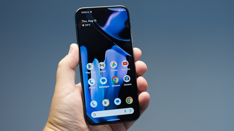 A Google Pixel 9 being held up to show its home screen and preinstalled apps