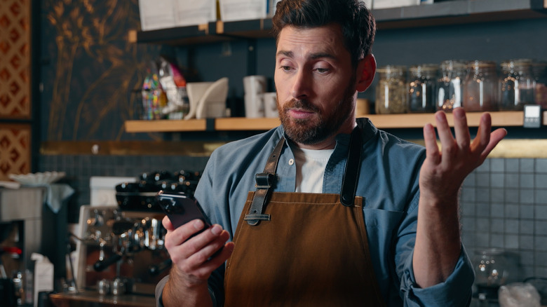 man frustrated and looking at phone while holding up hand in a gesture that implies confusion