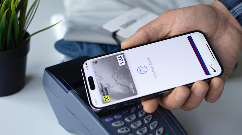 An iPhone with Apple Pay open on the display tapping a card reader.