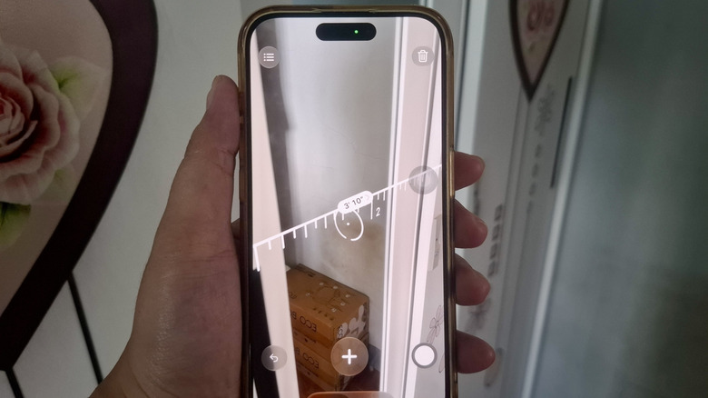 Hand holding iPhone with Measure app overlaying a measurement over a wardrobe