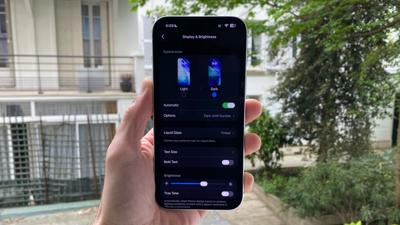A hand holding an iPhone. In the display, Display & Brightness adjustments