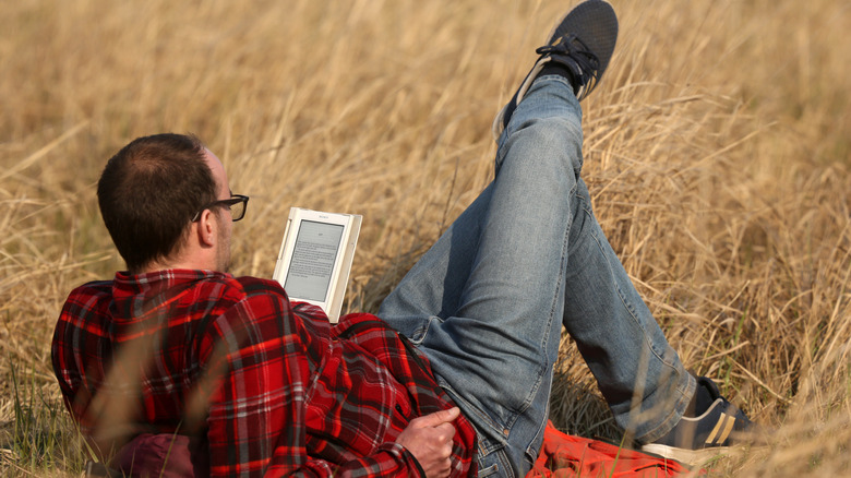 A man dressed in a red flannel and jeans lounges in a field of straw with an e-reader
