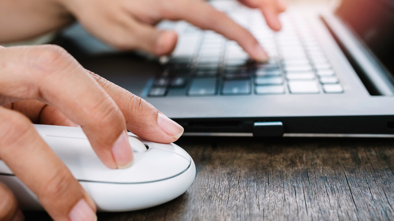person using a mouse with one hand and typing on a laptop with another