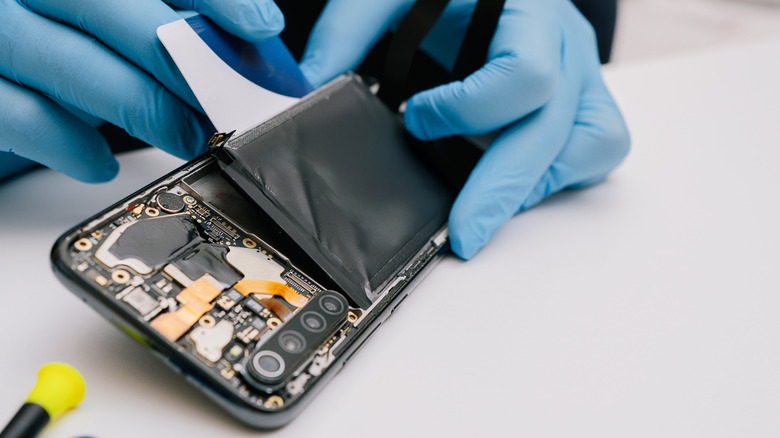 Someone replacing a battery in a smartphone with the back cover removed.