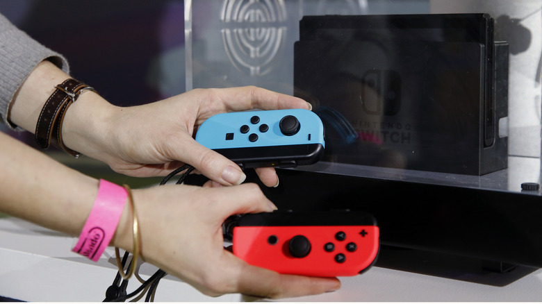 A person holding Joy-Cons in front of a Nintendo Switch console