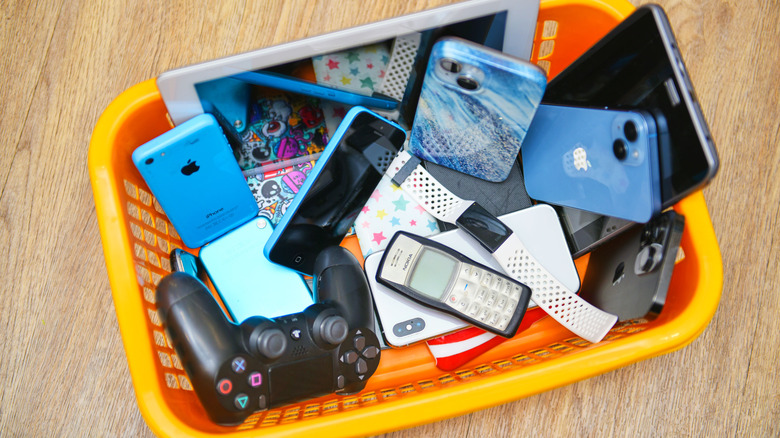 A pile of electronics, including phones, tablets, and controllers, are thrown into an orange garbage can.
