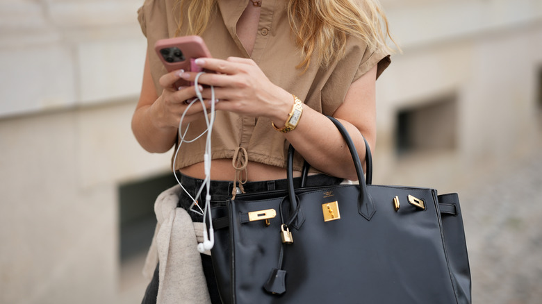 A woman holding a bag, phone, and wired earbuds.