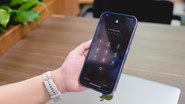 A person's hand holding a phone showing a keypad to enter a passcode