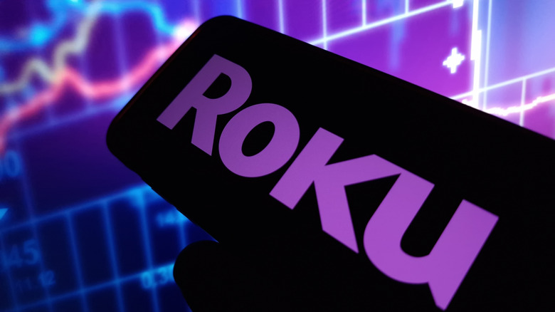 The Roku logo on a black smartphone screen set against a blue and purple backdrop.