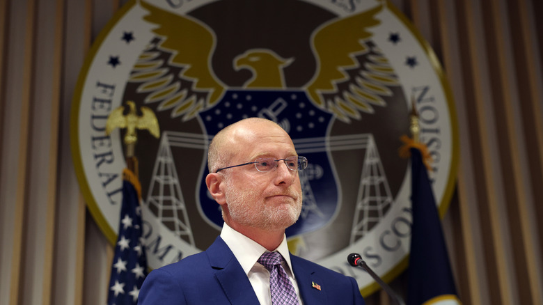 FCC Chairman Brendan Carr stands before his commission's seal during a press conference.