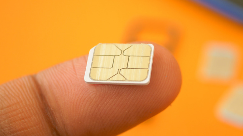 a person's finger holding up a SIM card with a phone in the background