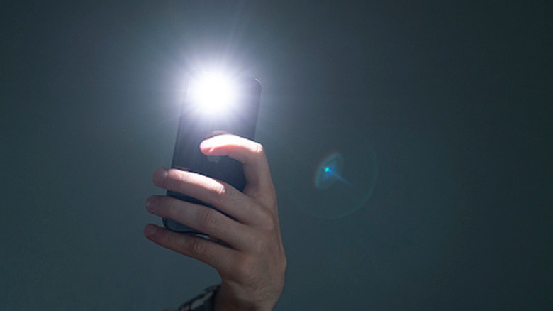 Hand holding a smartphone with the flashlight on