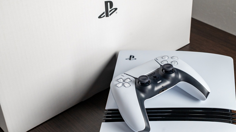 A Sony PS5 with a controller on top in front of a white box with the PlayStation logo on it