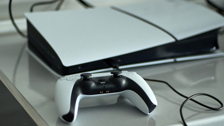 A PlayStation 5 likely sitting upside down as it on a silver countertop, the controller is prominent in front of the system