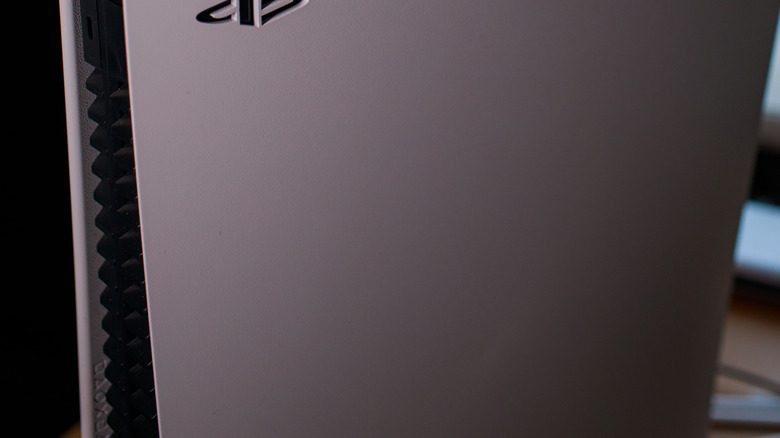 A PlayStation 5 controller is pictured sitting on top of a vertically placed PlayStation 5 console.