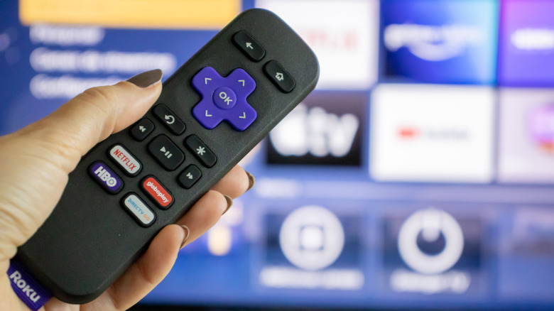 A person holding a Roku remote with a smart TV in the background