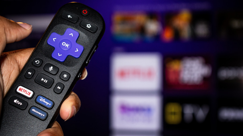A hand holding out a remote to control a Roku TV