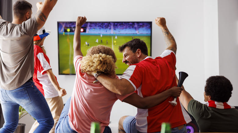 A group of people all watching sports on TV together and celebrating.