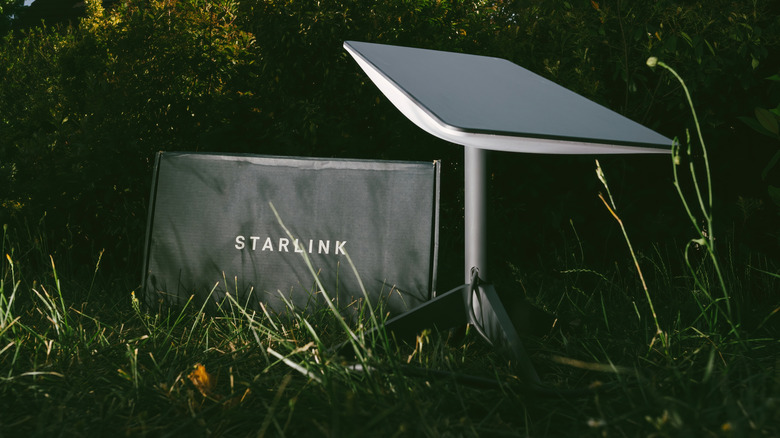 A Starlink satellite and kit sit side-by-side in a back yard.