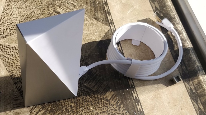 A Starlink Gen 1 router stands upright with its power cord coiled atop a table.