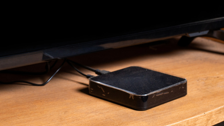 A black streaming media device sitting on a table in front of a TV