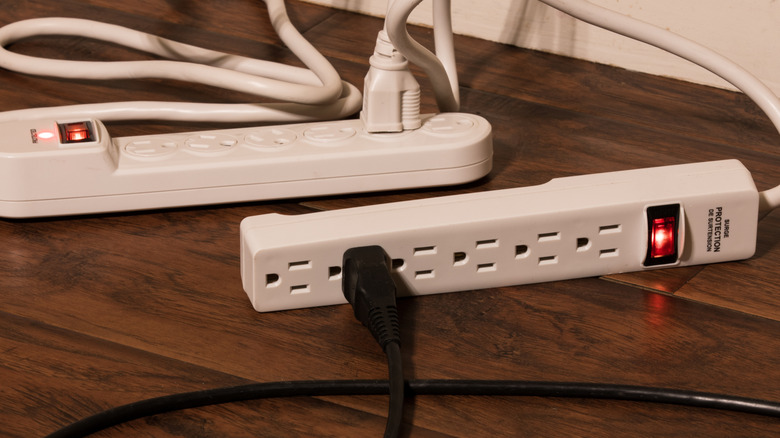 Two white six-outlet surge protectors with their red surge protection indicator lights on.