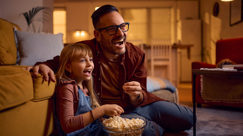 A father and daughter laughing at an off-screen TV