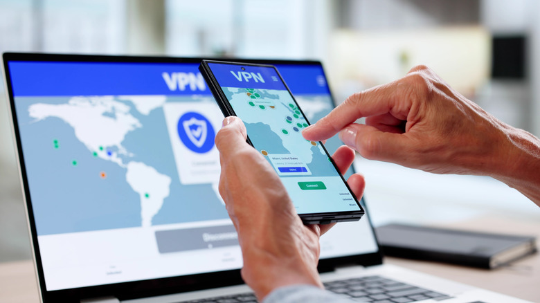 A person using a smartphone in front of a laptop with VPN details on both screens.