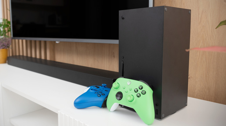 An Xbox Series X with two colorful controllers in front of it on a TV console
