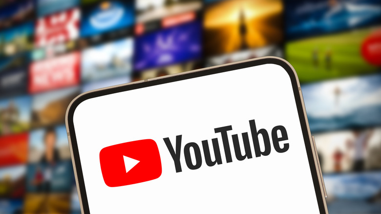 The YouTube logo appears on a smartphone screen, behind it is a heavily blurred background that looks like an array of YouTube title cards
