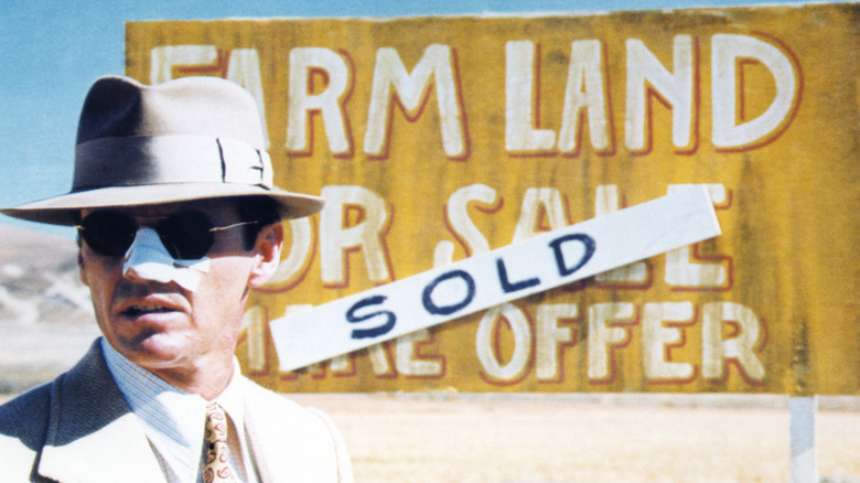 Detective Jake Gittes stares into the desert sun, his nose bandaged and his eyes shaded, before a yellow sign touting sold farmland.