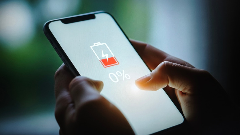 Person holding a smartphone with battery icon and percentage showing 0% charge.