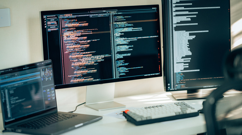 Dual monitors on a desk showing coding software where one of the monitors is oriented vertically
