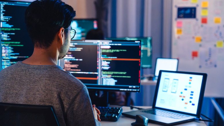 A desk work sitting at his desk with multiple displays coding and being productive