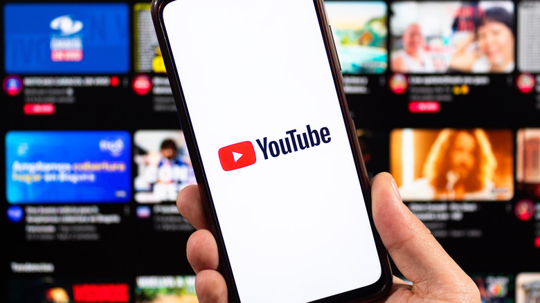 YouTube app open on smartphone in front of YouTube home page showing videos and streams