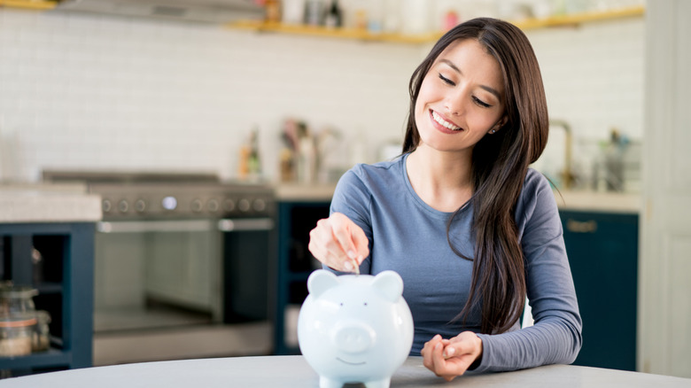 Woman putting coins into a piggy bank in a kitchen