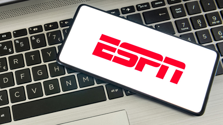 A smartphone displaying a red ESPN logo sits on top of a silver laptop that has black keys