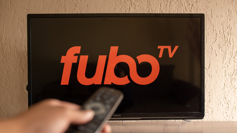The Fubo TV logo on a television with a person pointing a remote at it