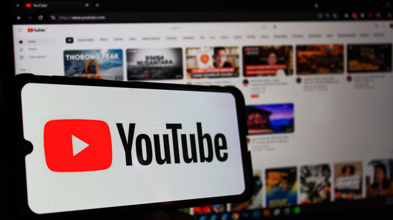 YouTube logo on a smartphone, and the YouTube website loaded on a laptop in the background.
