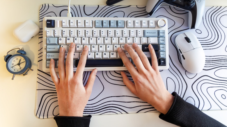 Image of a man's hand on a desk, showing a mouse and keyboard resting on a large desk mat.